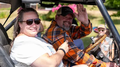 A couple smiles and waves from their open-top vehicle during the Fourth of July parade in Home, Washington.